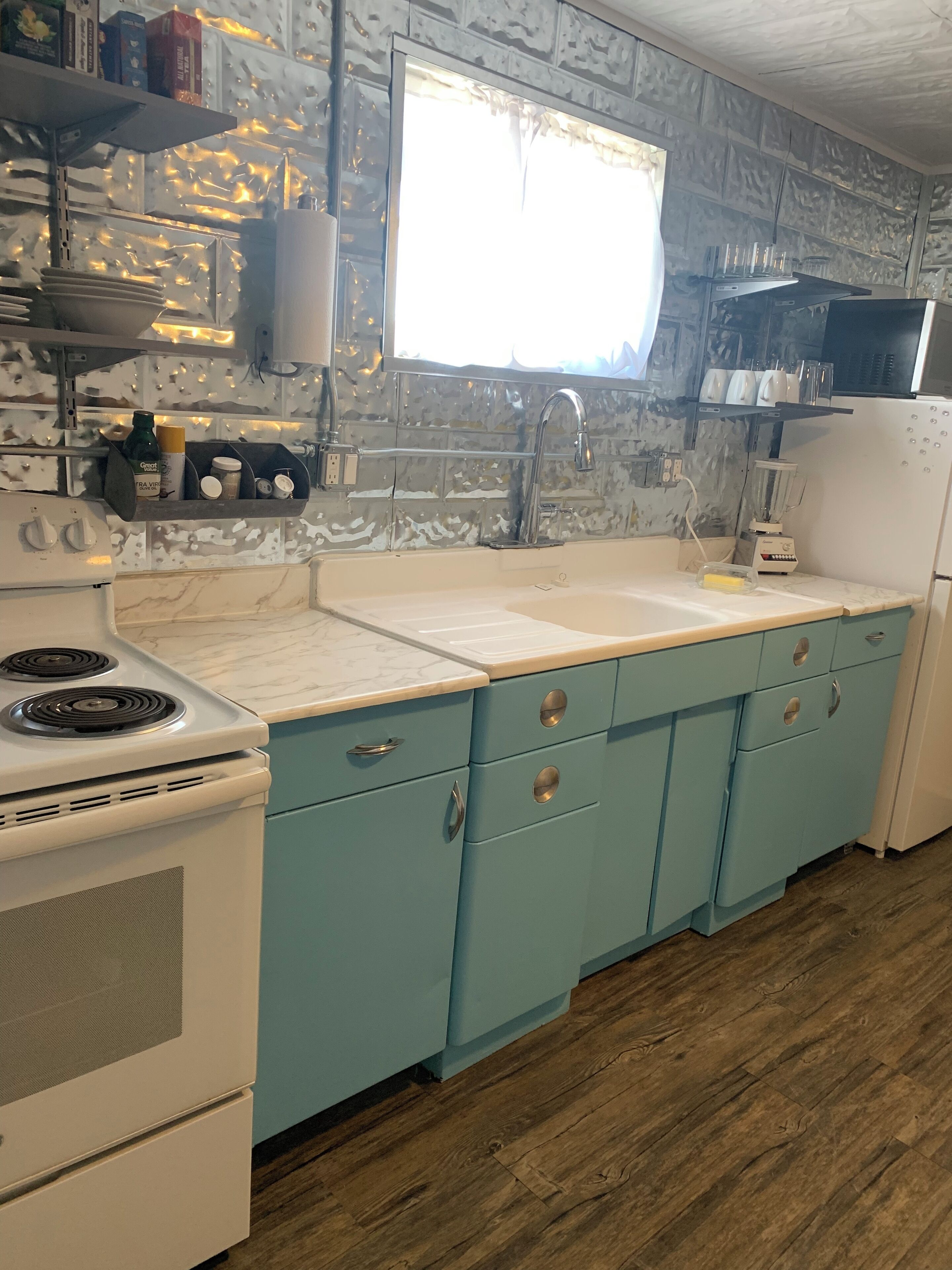 A kitchen with a white stove, a sink, and a refrigerator. There are cabinets with round handles and a window above the sink.
