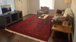 Ein Wohnzimmer mit einem roten, gemusterten Teppich, Holzmöbeln, einem Fernseher auf einem Schrank und einer Wandlampe.