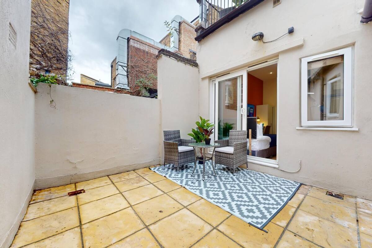 A small patio with a tiled floor, a patterned rug, wicker furniture, and a sliding glass door leading to a room.