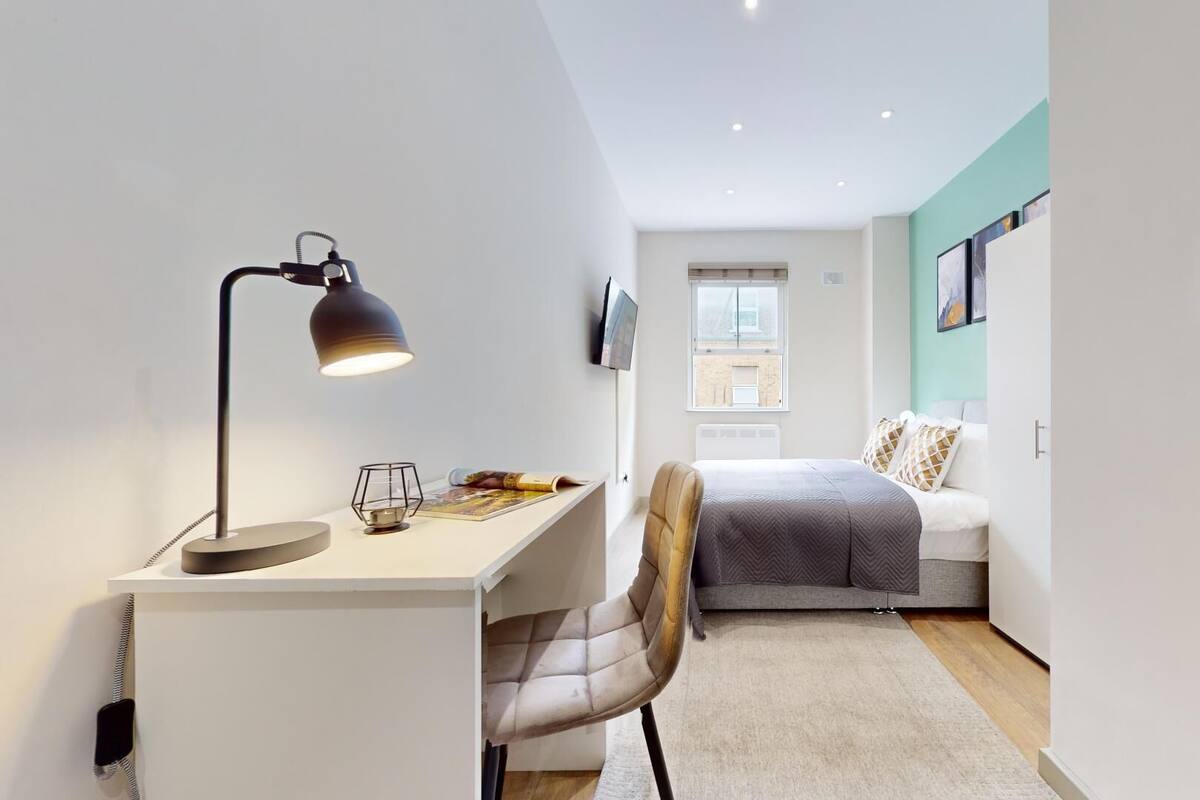 A modern, well-lit room with a desk, chair, and a bed with a view of the outside.