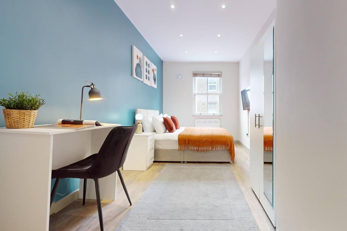 A modern bedroom with a desk, chair, bed, and a large mirror.