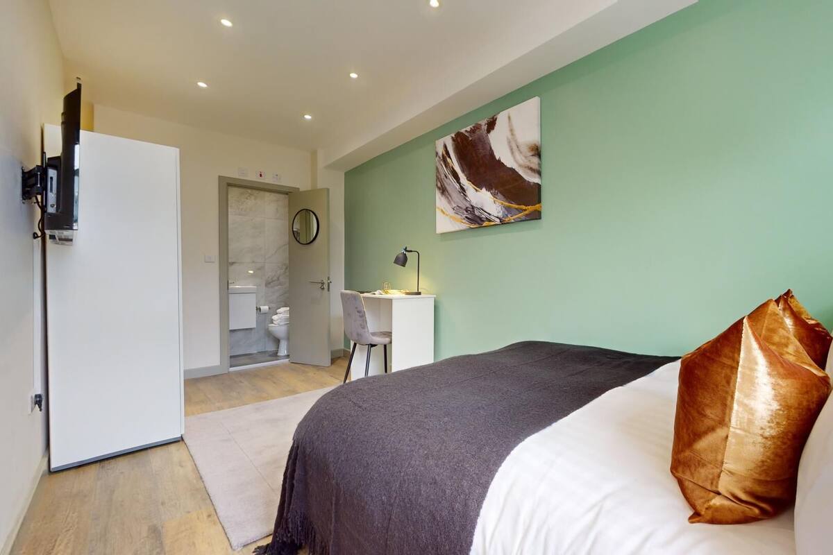 A bedroom with a bed, a desk, and a bathroom in the background.