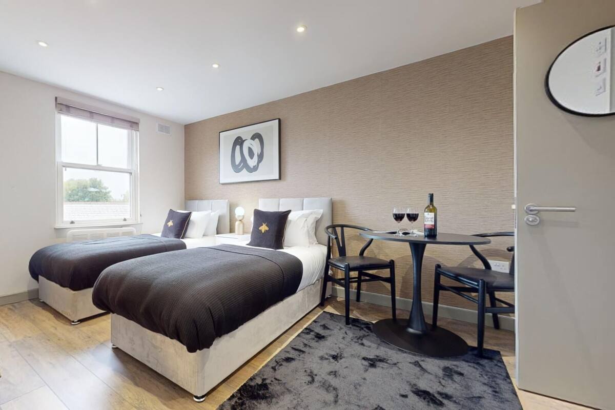 A modern hotel room with two beds, a desk, and a dining table.