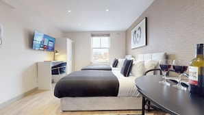 A modern hotel room with a bed, a desk, a TV, and a table with wine glasses and a bottle.