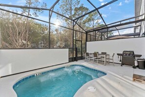 A swimming pool with a glass enclosure, surrounded by a patio area with outdoor furniture and a barbecue grill. - Lux 5BR Home w/Game Room, 4 Suites & Private Pool (Orlando)