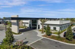 A modern building with a covered entrance, a parking lot, and landscaped areas with trees and shrubs. - Lux 5BR Home w/Game Room, 4 Suites & Private Pool (Orlando)