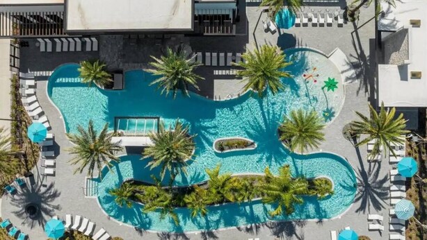 Eine Vogelperspektive eines Resorts mit einem zentralen Schwimmbecken, umgeben von Palmen und Liegestühlen.