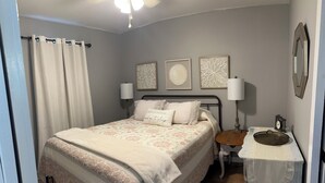 A bedroom with a bed, bedside lamps, a nightstand, a mirror, and wall art. - Little Southern Charm in tranquil Flovilla with AC, WiFi (Flovilla)