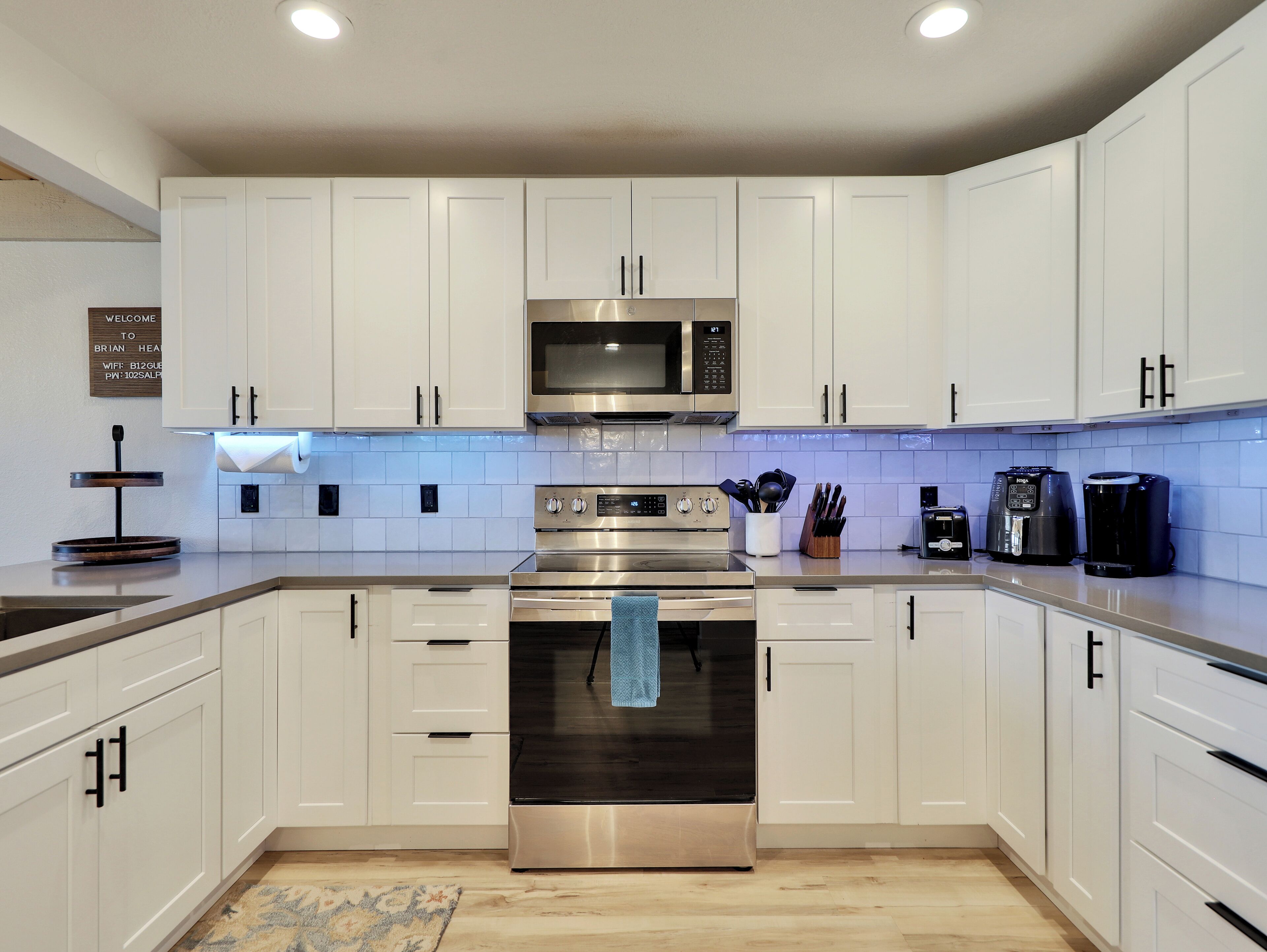 Cocina moderna con armarios blancos, electrodomésticos de acero inoxidable y una toalla azul colgada del horno.