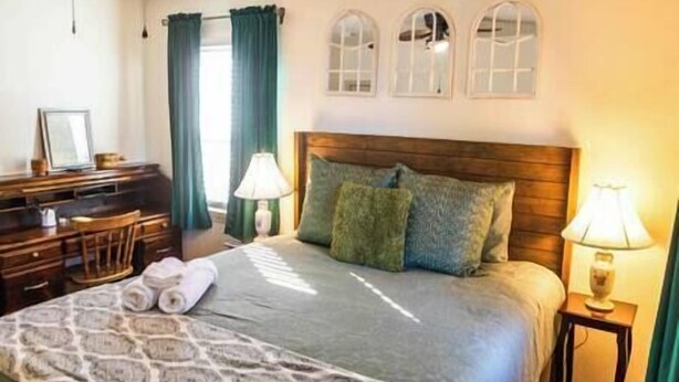 A hotel room with a bed, a desk, and a chair. There are three arched windows above the bed. - Tinker AFB OKC I-40 Colonial Dorchester Cottage (Midwest City)