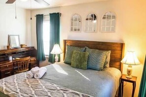 A hotel room with a bed, a desk, and a chair. There are three arched windows above the bed. - Tinker AFB OKC I-40 Colonial Dorchester Cottage (Midwest City)