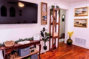 A room with a wooden desk, a potted plant, a clock, and framed pictures on the wall. - Model City Homes Stays: Tinker AFB OKC I-40 Colonial Dorchester Cottage (Midwest City)