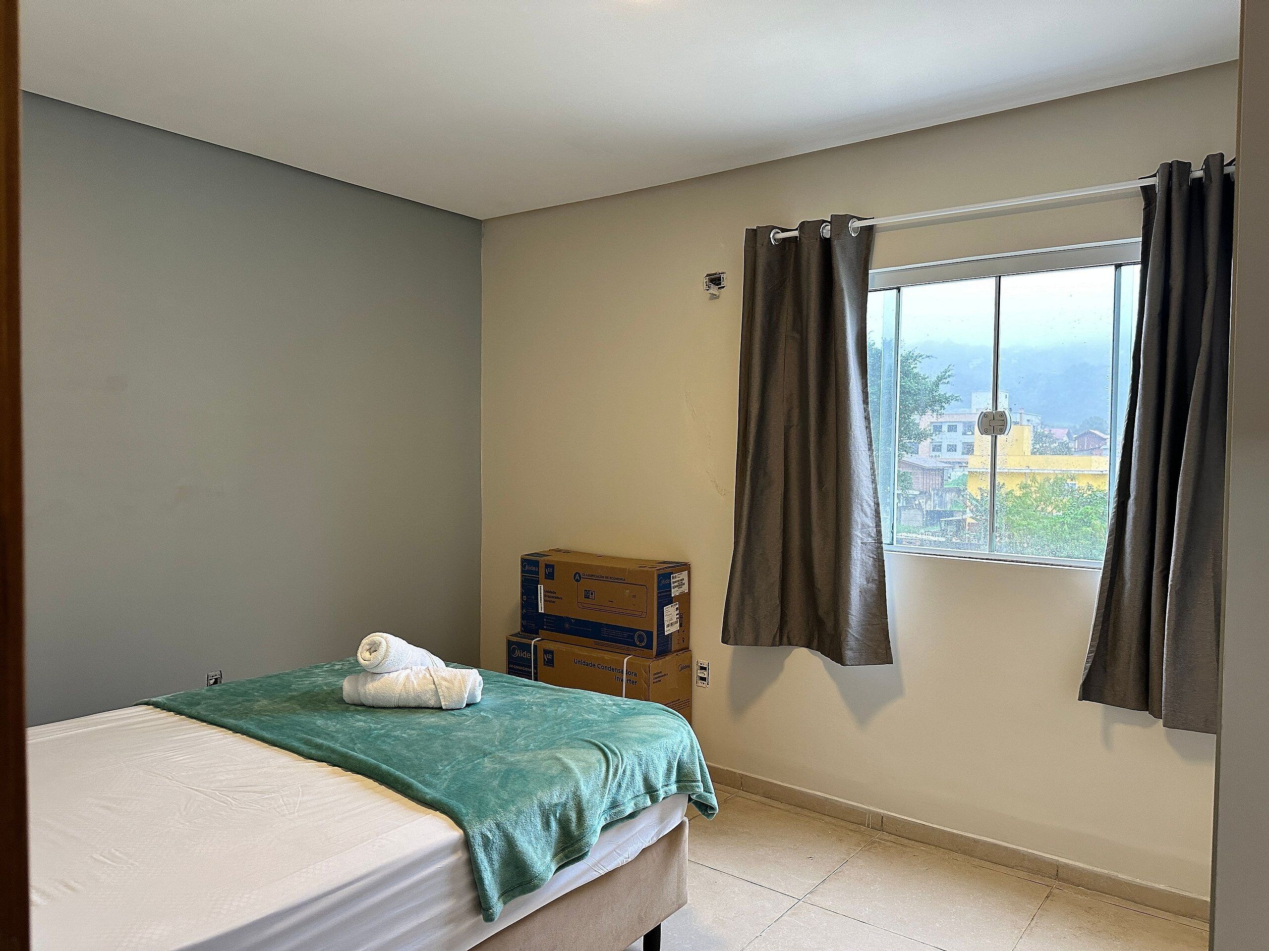 Ein Schlafzimmer mit einem Bett, einem Fenster mit Vorhängen und Blick auf Gebäude.