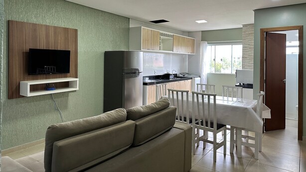 Een moderne keuken met een inbouwoven, een eethoek met een witte tafel en stoelen, en een woonkamer met een bank.
