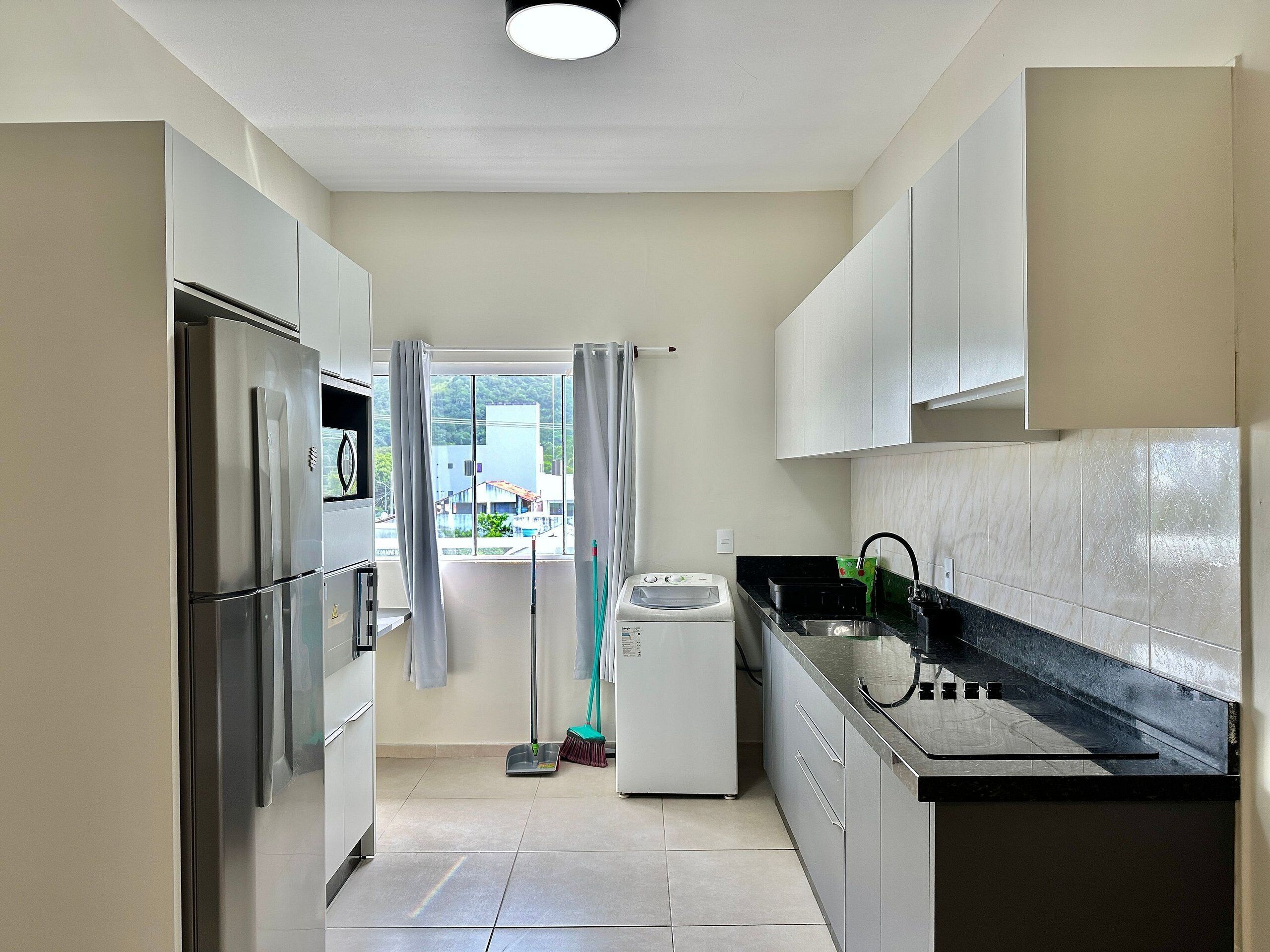Una cocina moderna con electrodomésticos de acero inoxidable, lavadora y vista a un barrio residencial.