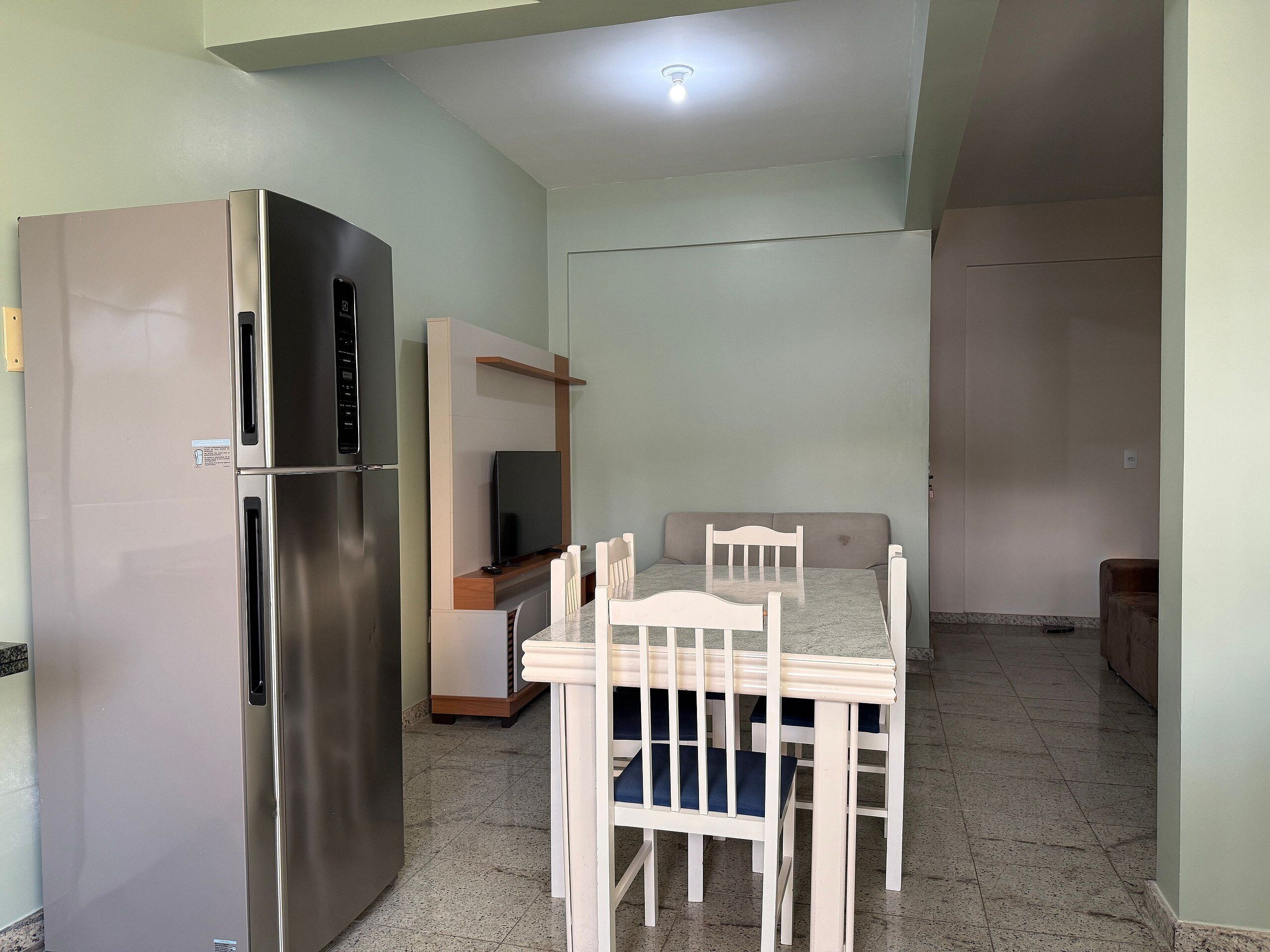 A compact kitchen with a built-in refrigerator, a dining table with chairs, and a television on a stand.
