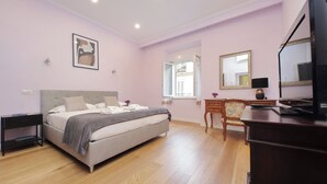 A bedroom with a bed, bedside tables, a dresser, a mirror, and a television.