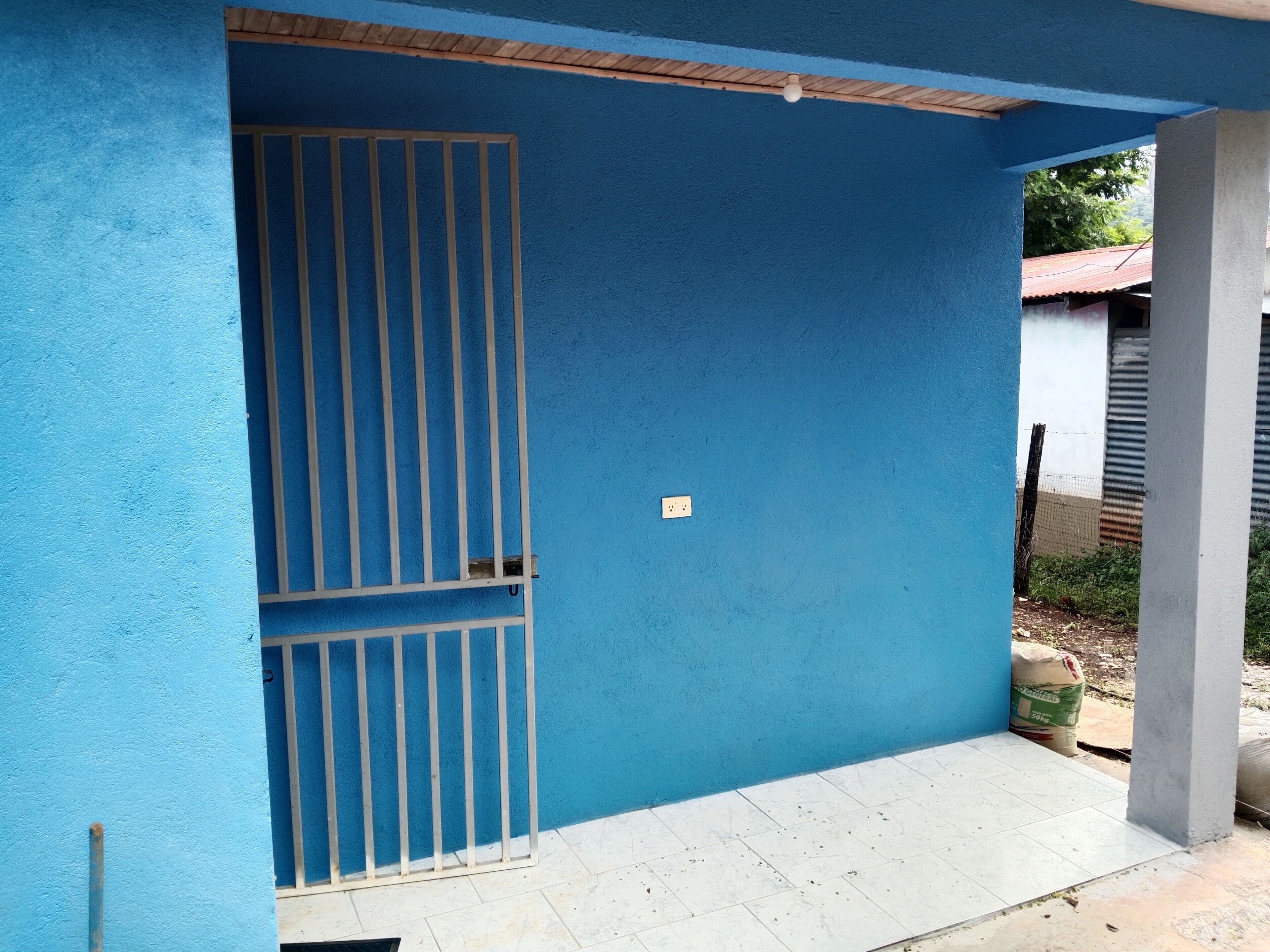A blue exterior wall with a metal gate, a tiled floor, and a concrete pillar.