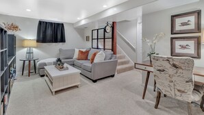 A modern living room with a grey sofa, white coffee table, and a patterned armchair. A staircase leads to another level, and there are framed pictures on the wall. - Mountain Views , Skiing, Lake & Coffee Bar (Ogden)
