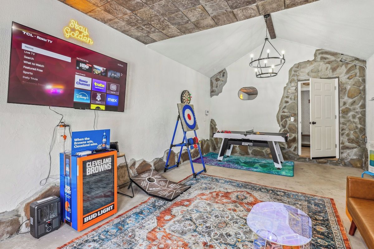 Une pièce avec un téléviseur fixé au mur qui affiche l’interface d’un service de diffusion en continu, un jeu de fléchettes, une table de baby-foot et un tapis à motifs.