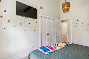 A bedroom with a bed, a television mounted on the wall, and a door leading to another room.