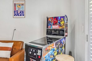 A room with a brown leather sofa, a small wooden table, and a wall-mounted arcade machine featuring Marvel characters.