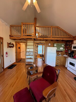 Un vaste espace de vie comprenant un escalier en bois, une table à manger, un fauteuil rouge et une cuisine équipée d’un réfrigérateur et d’une cuisinière.