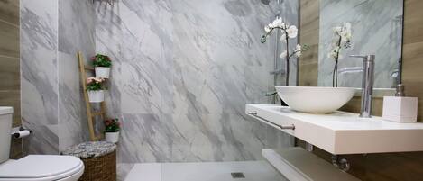 A modern bathroom with a white toilet, a large white sink, and a shower area.