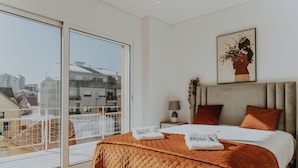 Un dormitorio moderno con una cama grande, vista a la ciudad a través de una puerta corredera y una obra de arte enmarcada en la pared.