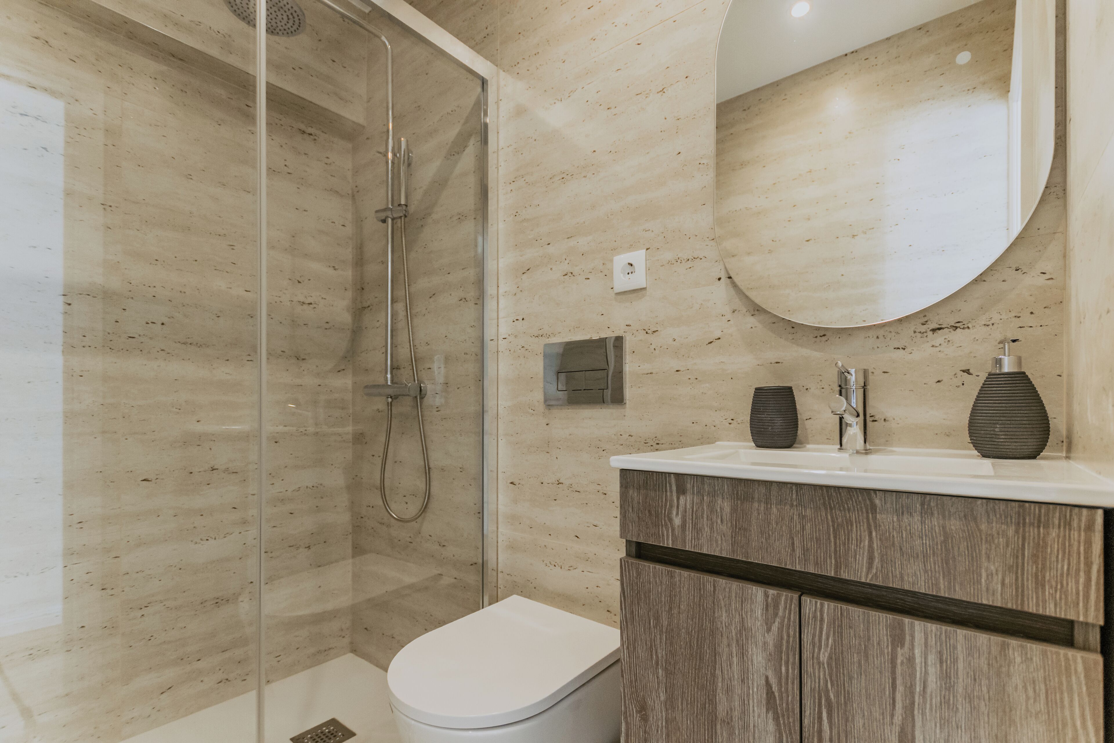 A modern bathroom with a glass-enclosed shower, a white toilet, and a wooden vanity with a mirror.
