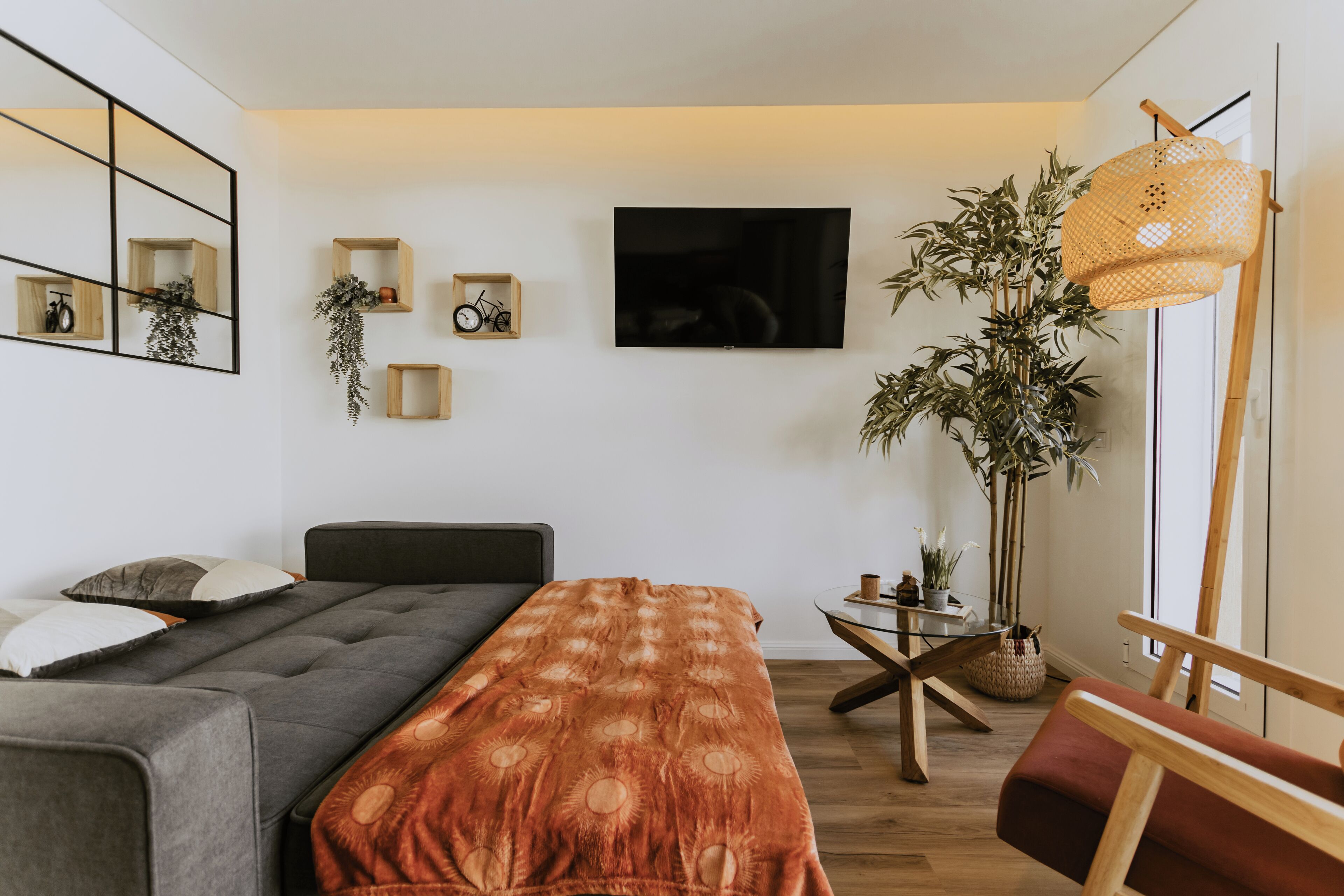 Ein modernes Schlafzimmer mit Bett, Fernseher, Pflanze und einem Holznachttisch.