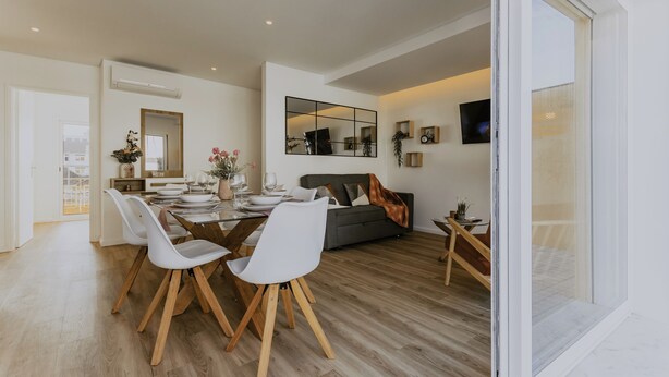 Una sala de estar moderna con comedor, que incluye un sofá, una mesa de centro y un televisor instalado en la pared.