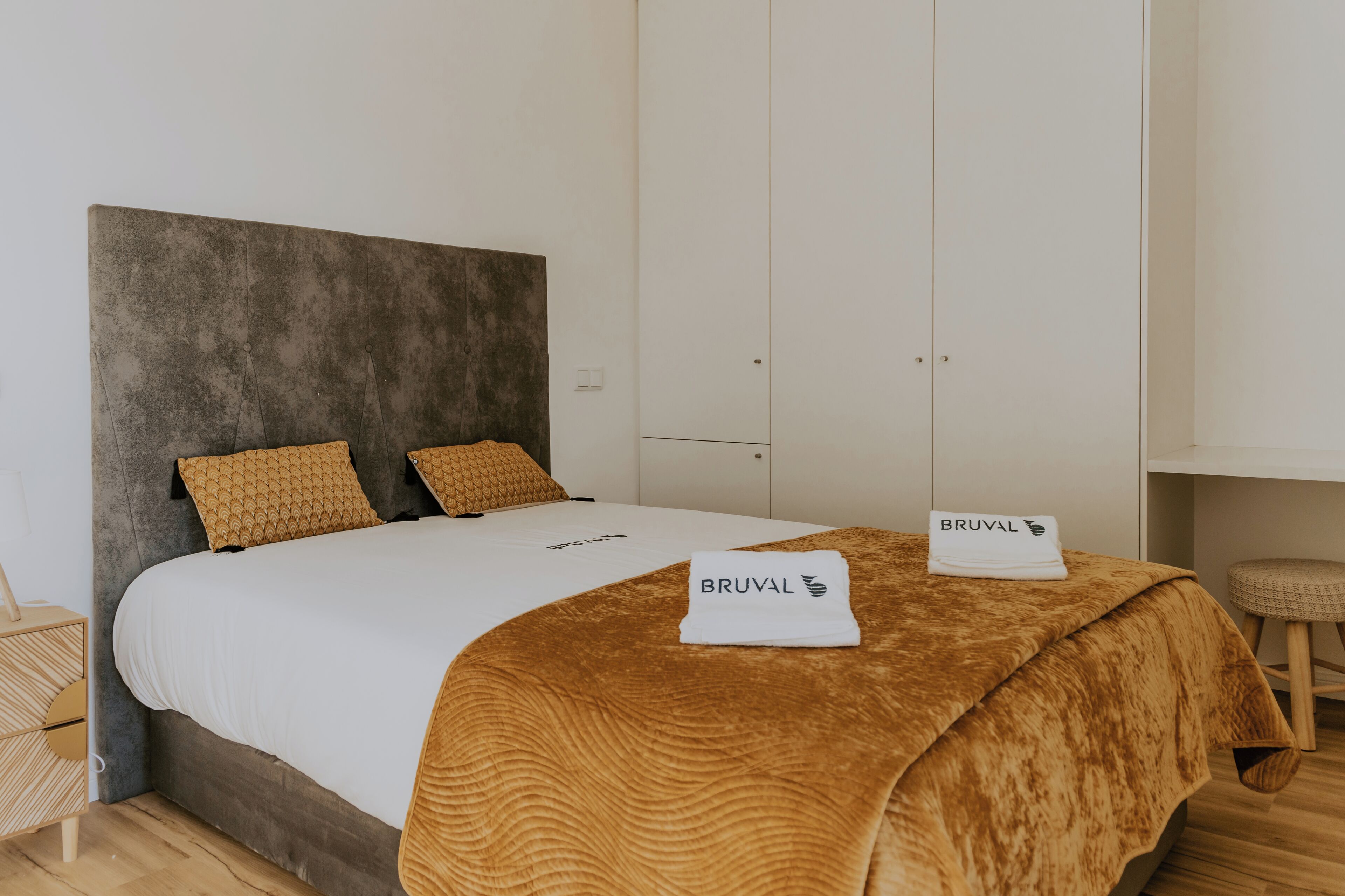 Un lit bien fait, avec une couverture marron et deux oreillers, une tête de lit blanche et une armoire blanche avec une porte.
