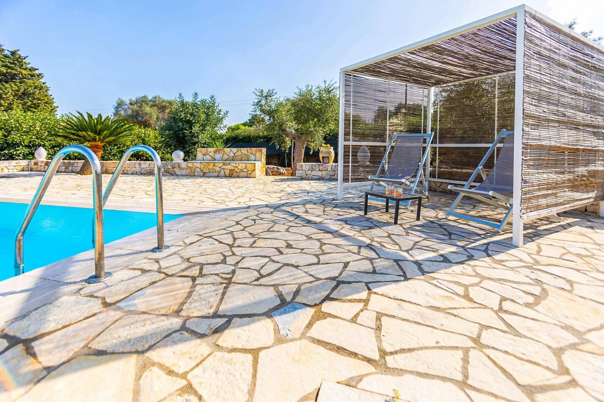 Zona de piscina con suelo de piedra, un espacio de estar cubierto y una escalera de piscina.
