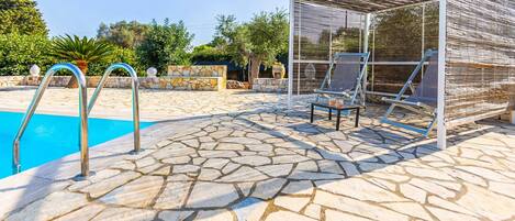 Zona de piscina con suelo de piedra, un espacio de estar cubierto y una escalera de piscina.