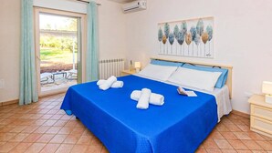 A hotel room with a bed, a window with curtains, a radiator, and a painting on the wall.