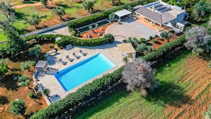 An aerial view of a property with a swimming pool, a covered patio, and a house with a tiled roof.