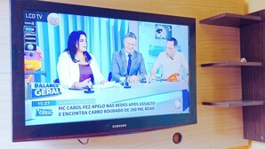 Een Samsung LCD-televisie bevestigd aan een gele muur, waarop een nieuwsuitzending wordt vertoond.