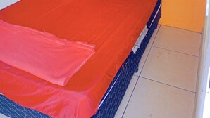 Een bed met een rode sprei en twee kussens, een gestapeld hoofdbord, en twee ingekaderde foto's aan de muur.