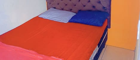 A bed with a red bedspread and two pillows, a tufted headboard, and two framed pictures on the wall.