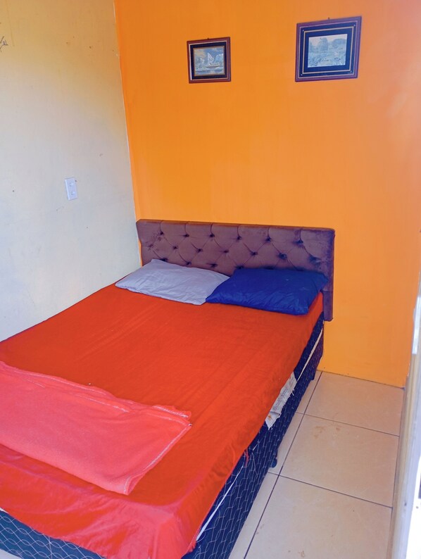 A bed with a red bedspread and two pillows, a tufted headboard, and two framed pictures on the wall.