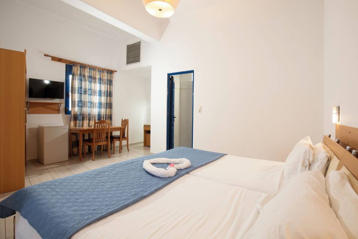 A hotel room with a bed, a desk, a chair, a TV, and a bathroom door.