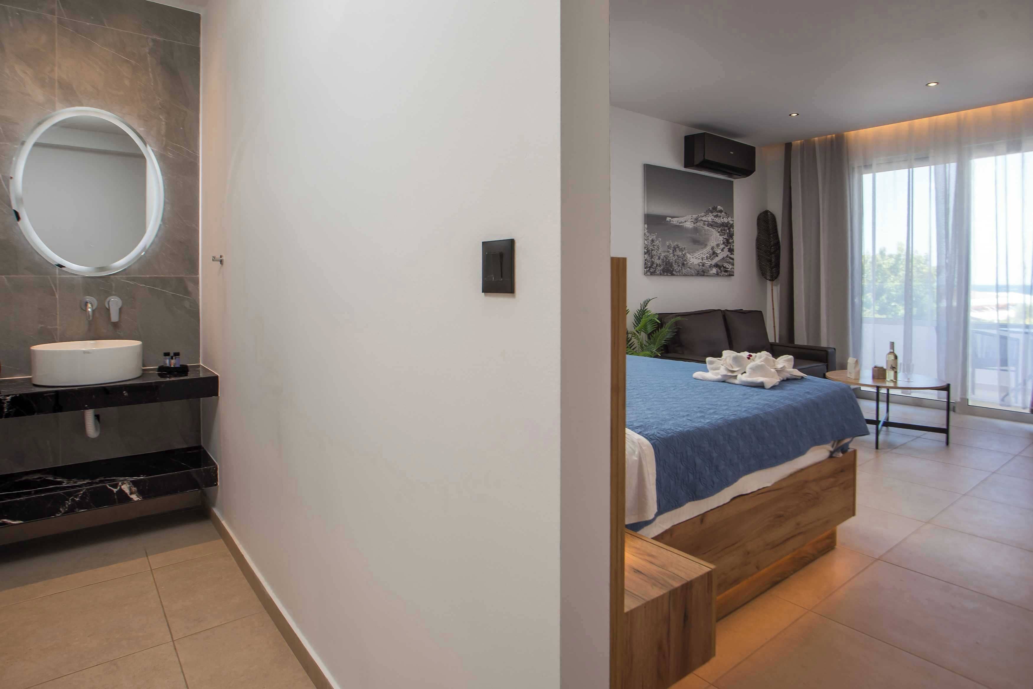 Une chambre à coucher moderne, avec un lit, une table de chevet, une grande fenêtre et une salle de bain équipée d’un lavabo et d’un miroir.