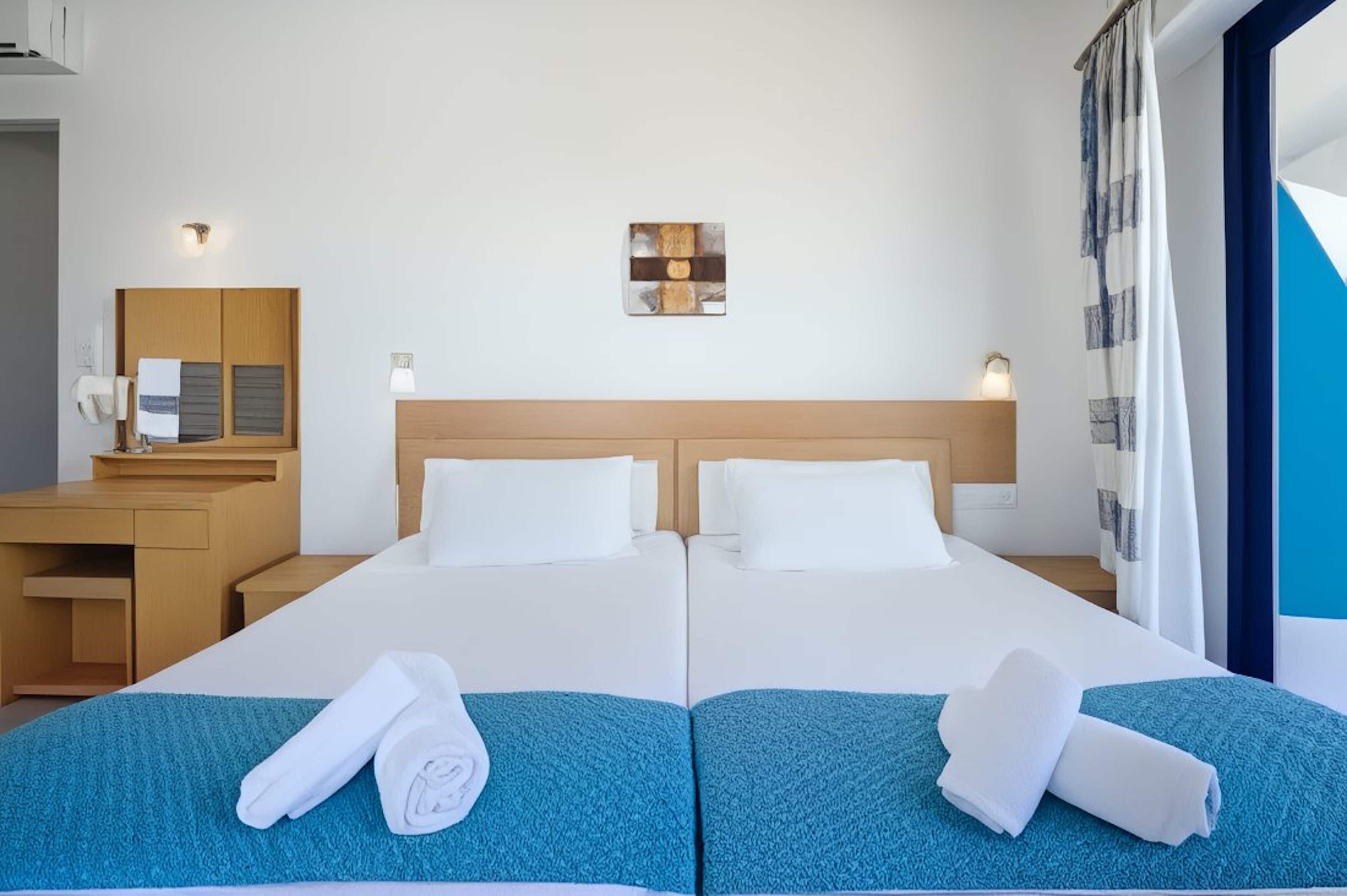 A hotel room with two beds, a wooden headboard, a desk with a chair, a mirror, and a wall-mounted light fixture.