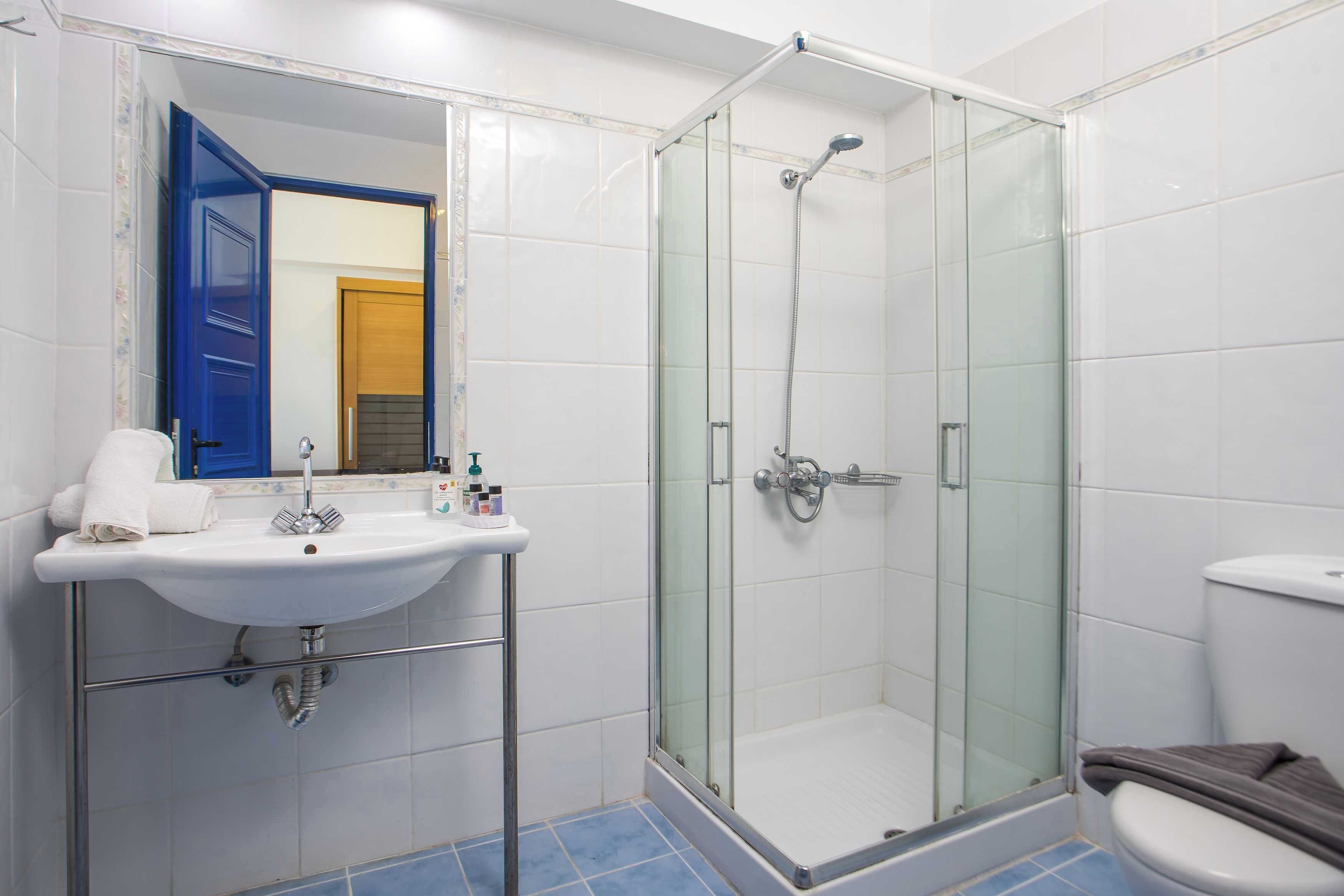 A bathroom with a glass-enclosed shower, a white sink, and a blue-tiled floor.