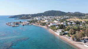 A coastal town with a beach, clear blue waters, and buildings along the shore. - RAFFAELLO BEACH (Rhodes)