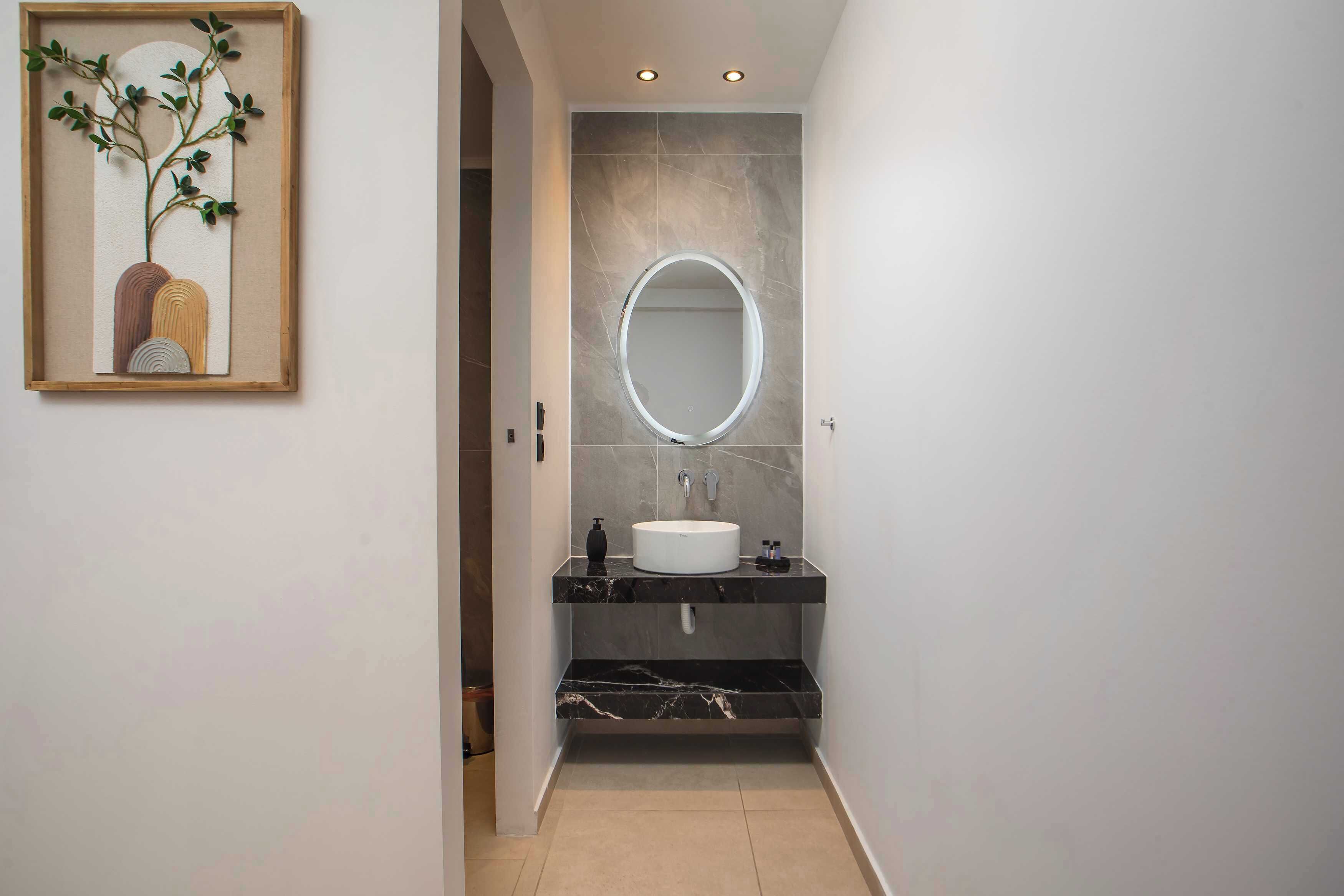 A modern bathroom with a marble vanity, a round mirror, and a framed artwork on the wall.