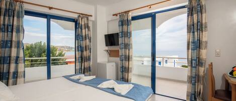 A hotel room with a bed, curtains, a TV, and a balcony with a view.