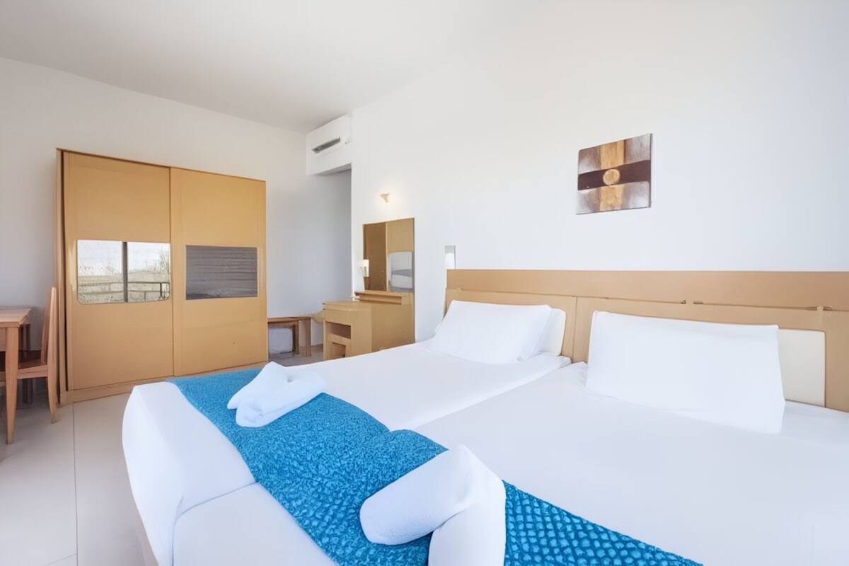 A hotel room with a large bed, a desk, a wardrobe, and a mirror.