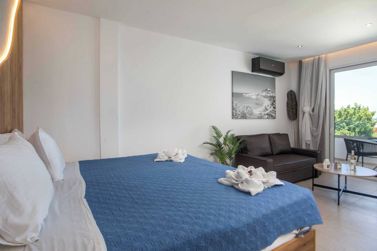 A hotel room with a bed, a sofa, a small table, and a balcony.